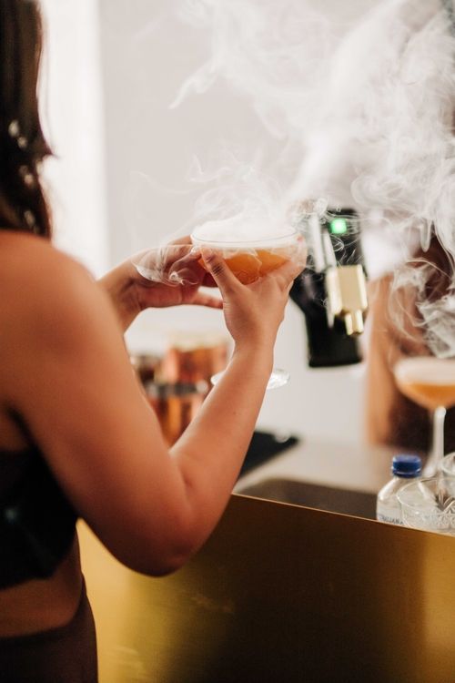 Hand holding a cocktail glass with smoke effects in dark lighting.