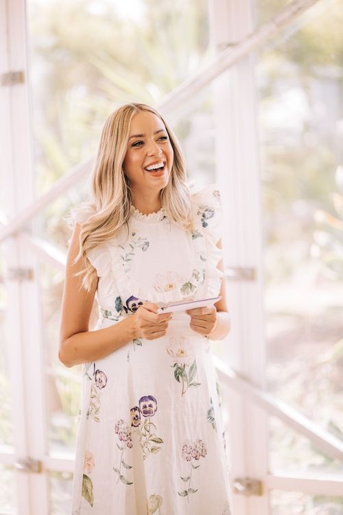 Woman in white floral dress laughing joyfully in bright natural light.