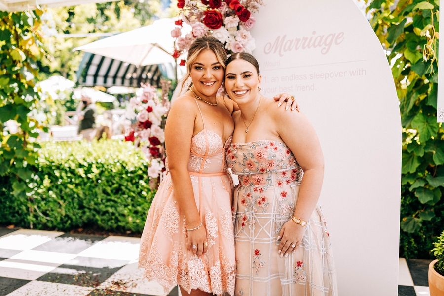 Two women in pink floral dresses posing together at an outdoor event.