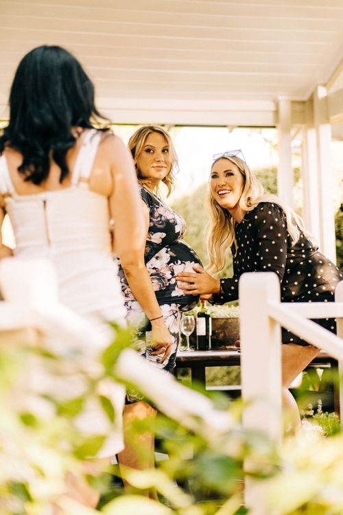 Friends enjoying a casual outdoor gathering on a sunny porch with joyful expressions.