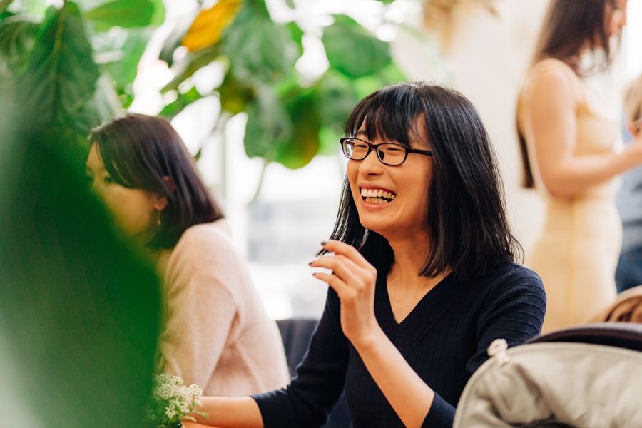 A woman laughs joyfully during a social gathering with plants in the foreground.