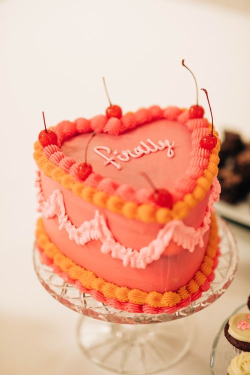 Pink heart-shaped cake decorated with cherries and piped frosting details.