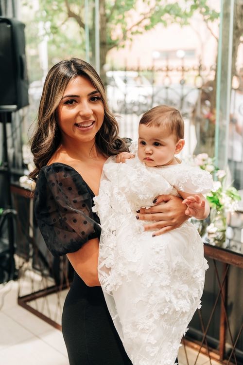 Adult holds baby wearing white lace christening gown during special occasion celebration.
