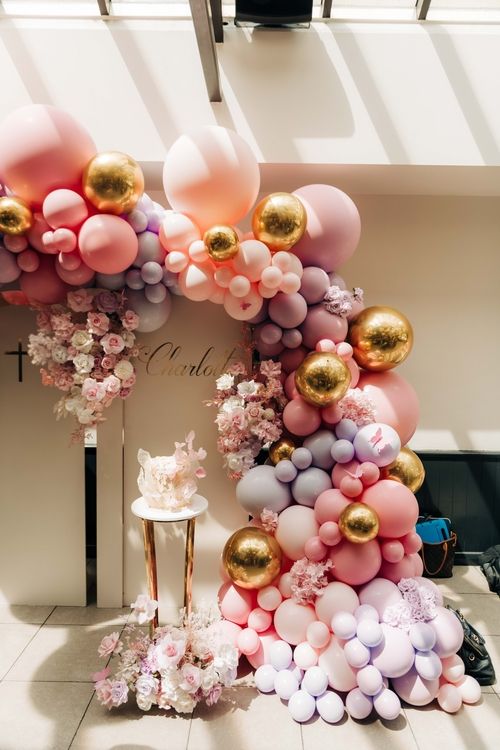 Luxurious balloon arch with pink and gold balloons decorated with flowers for celebration.