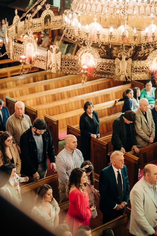 Church congregation gathered in wooden pews under ornate crystal chandeliers during a special ceremony.