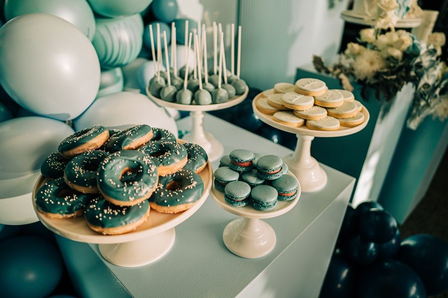 Elegant dessert display featuring donuts and treats on white cake stands with balloons.