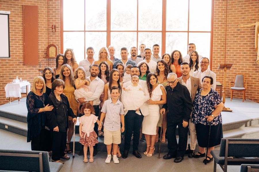Large group photo of celebration attendees in formal attire inside modern church space.