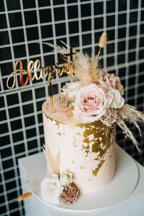 Elegant pink and gold celebration cake decorated with dried flowers and custom name topper.