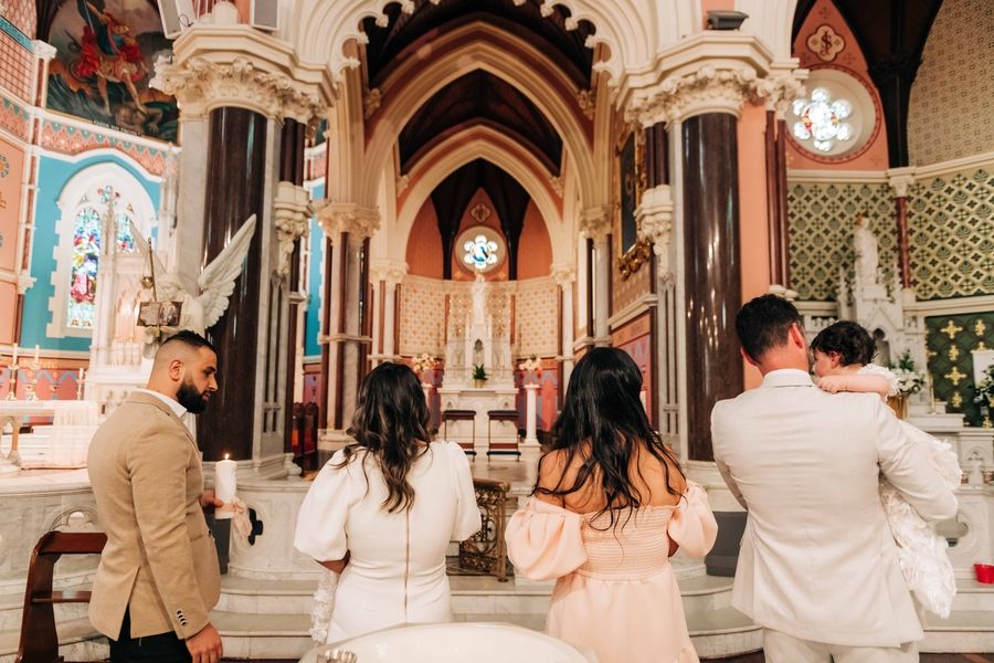 Several people stand in a beautifully ornate Catholic church with gothic arches and decorated walls.