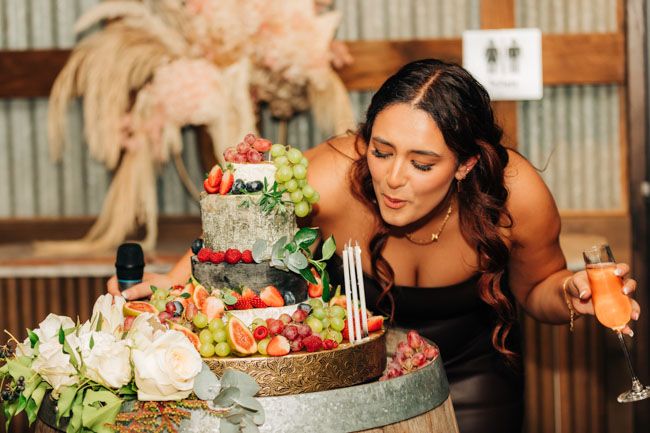 A beautifully decorated celebration cake with fresh flowers and fruit sits on a rustic table.