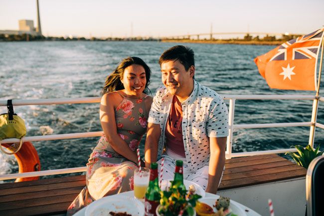 Couple enjoying drinks on a boat with Australian flag at sunset.