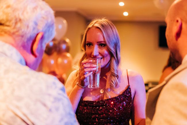 Person enjoying a drink while socializing at an indoor event with warm lighting.