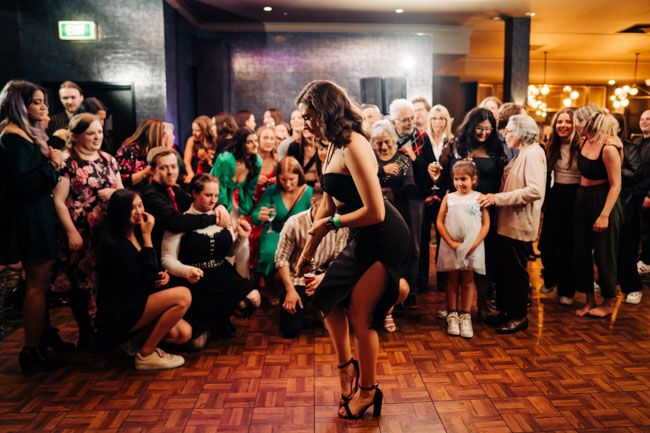 Crowd watches as someone dances on a wooden floor during a party.