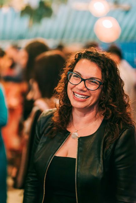 Woman in leather jacket and glasses smiling at social gathering.