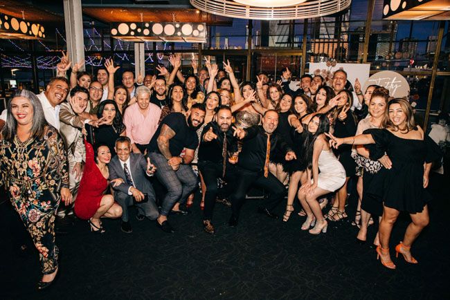 Large group photo of party guests dressed in black and festive attire.