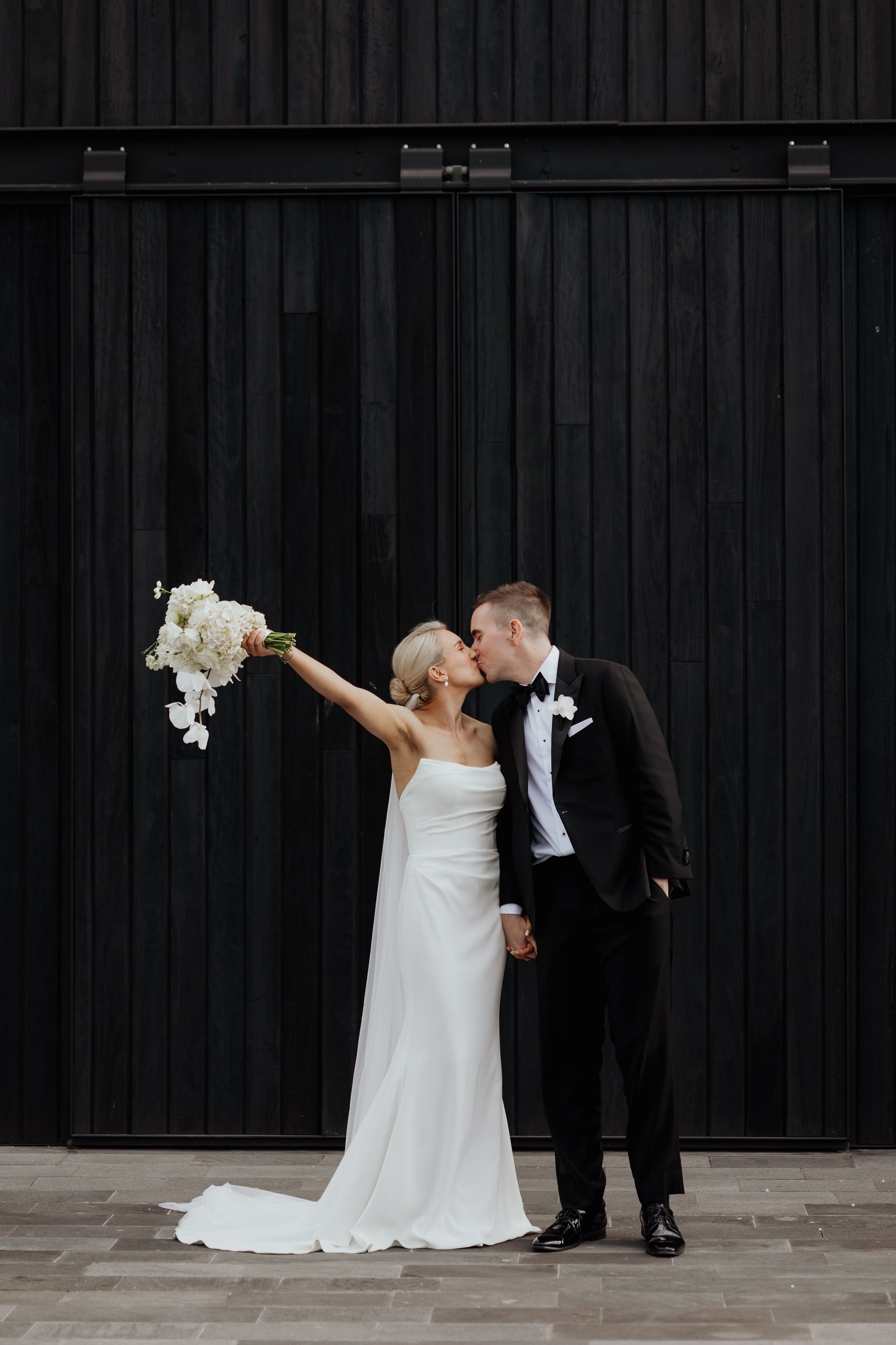 A newly married couple kiss and celebrate outside a dark building.