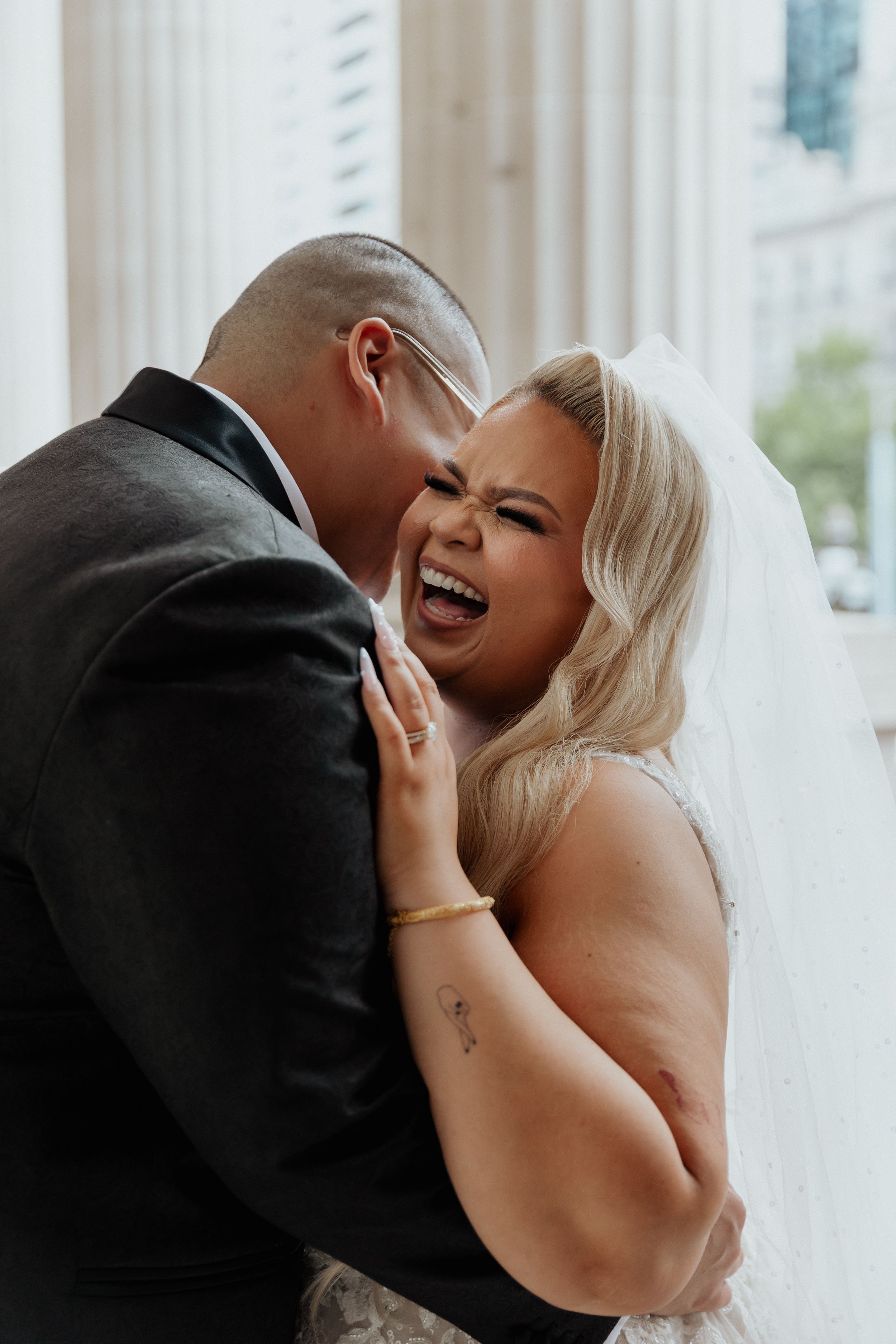 A bride and groom share a joyful laugh in a close portrait.