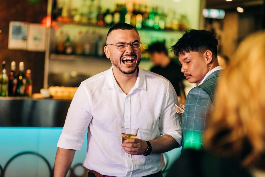 Person in white shirt laughing while holding drink at bar.