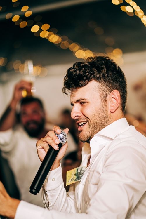 Person in white shirt singing into microphone at lively party.