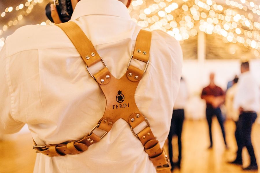 Close-up of leather camera harness straps worn over a white shirt at a party reception.