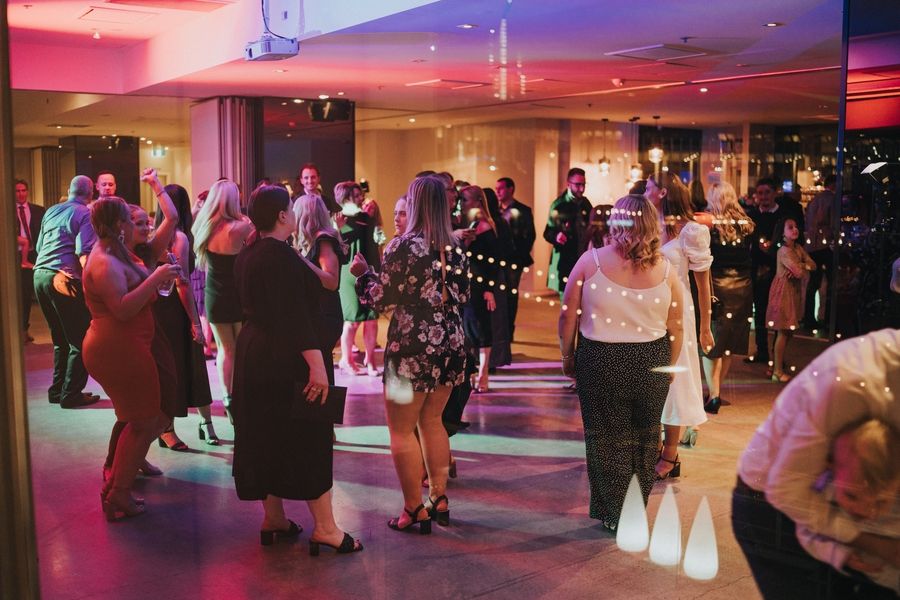 party reception dance floor with guests dancing under colorful lighting and string lights.