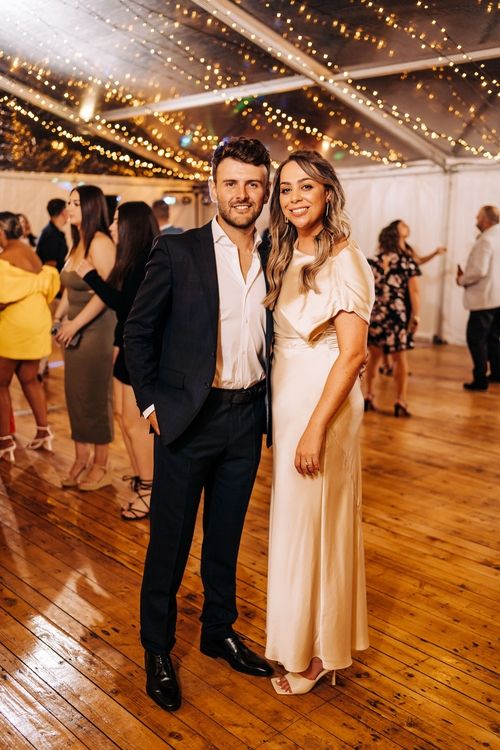 party reception venue decorated with string lights and guests dancing on wooden floor.