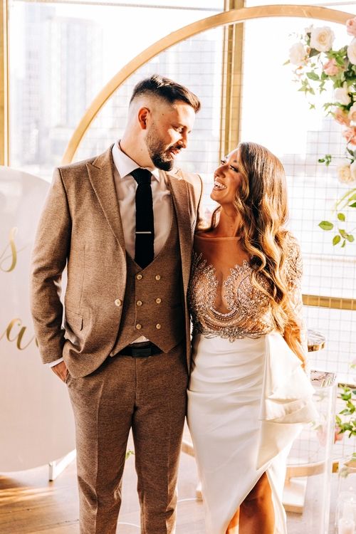 Elegant couple poses in formal attire against circular arch with floral decorations.