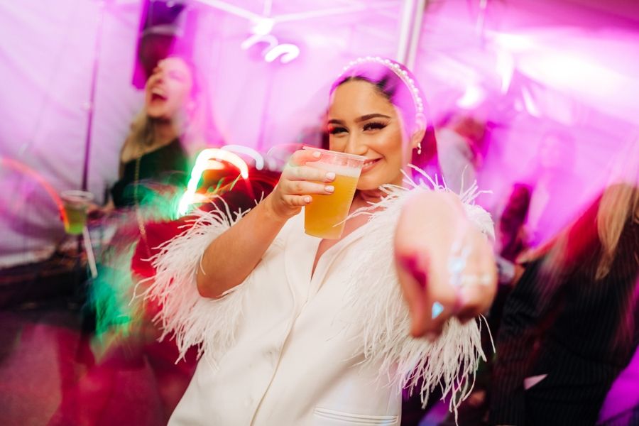Party scene with person in white feathered outfit under pink lighting.