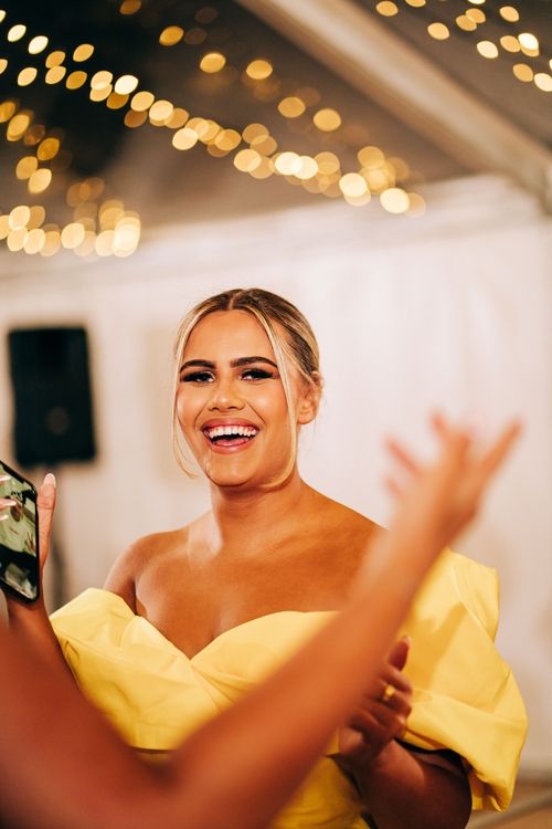 A person in a yellow off-shoulder dress laughs joyfully under twinkling lights.