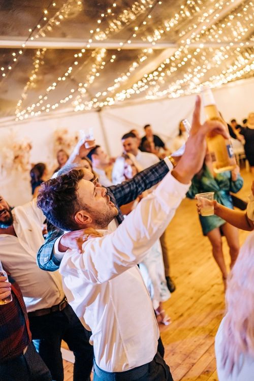 A person dancing enthusiastically with raised arms under string lights at a celebration.
