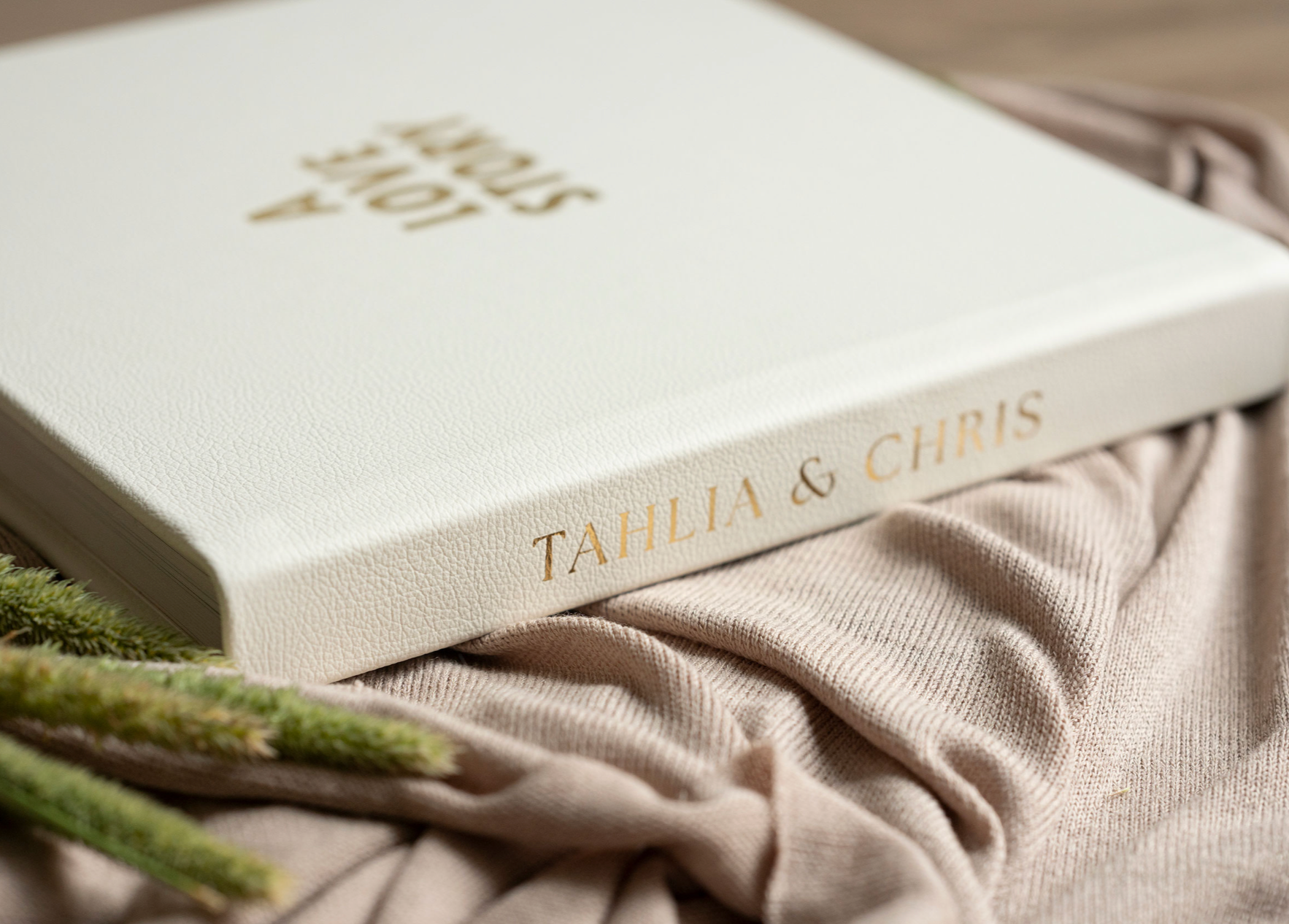 A white wedding album titled Love Story rests beside greenery.