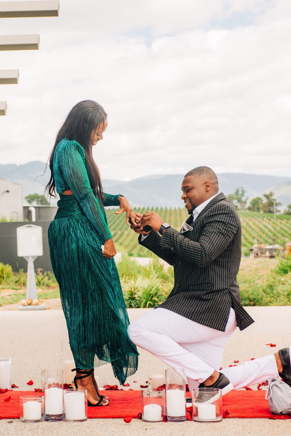 Marriage proposal scene with red candles on a terrace overlooking vineyard countryside.