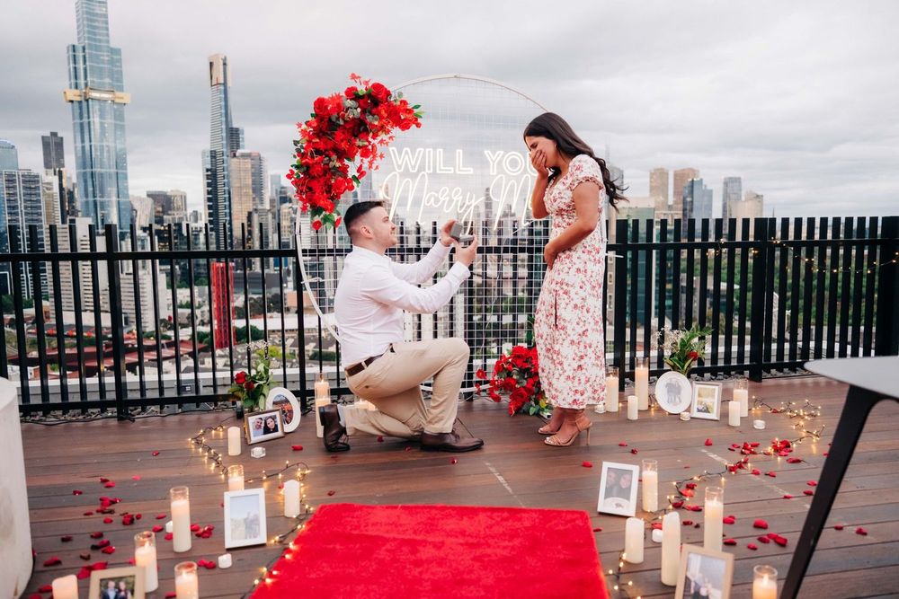 Rooftop proposal scene with red roses and candles against city skyline.