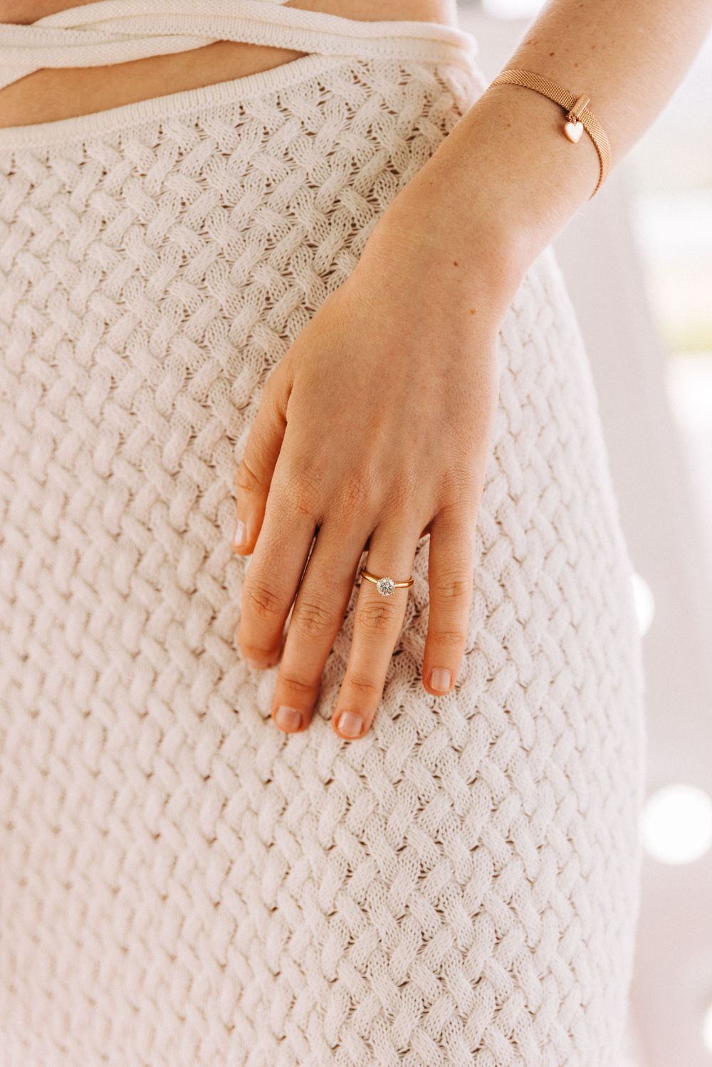 Close-up of a hand wearing delicate rings against a white textured fabric background.