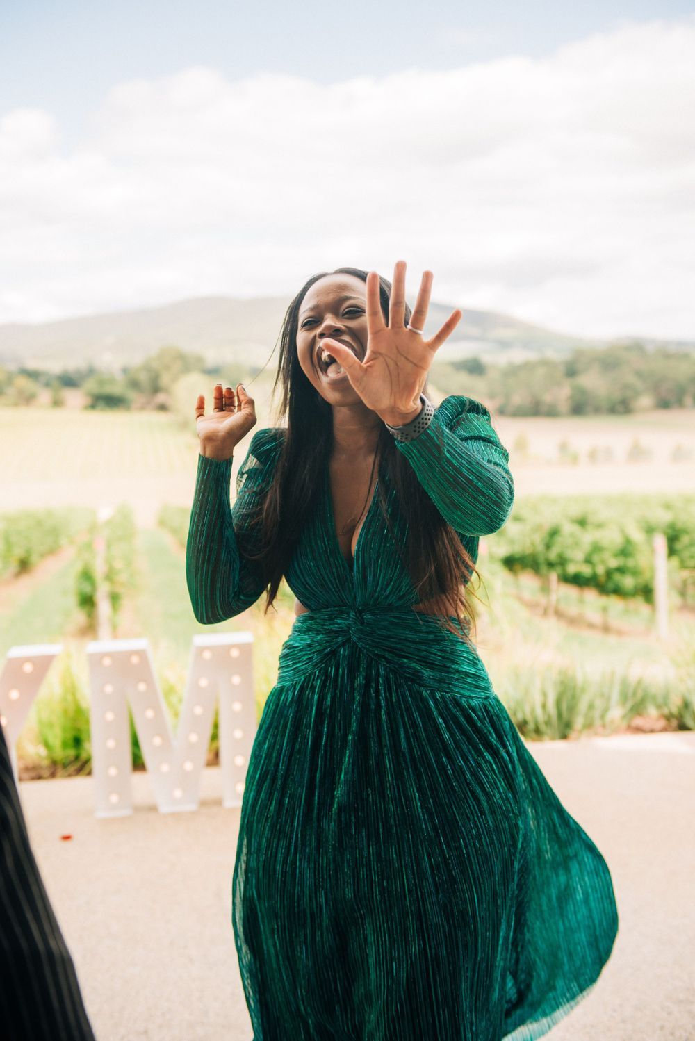 Woman in emerald green dress showing off engagement ring with excitement.