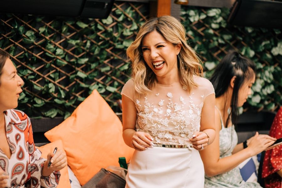 Woman in lace dress laughing with friends at an outdoor gathering.