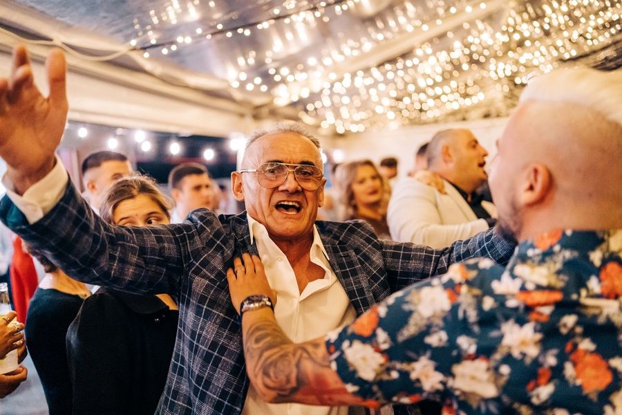 An energetic party scene with guests celebrating under crystal chandeliers.