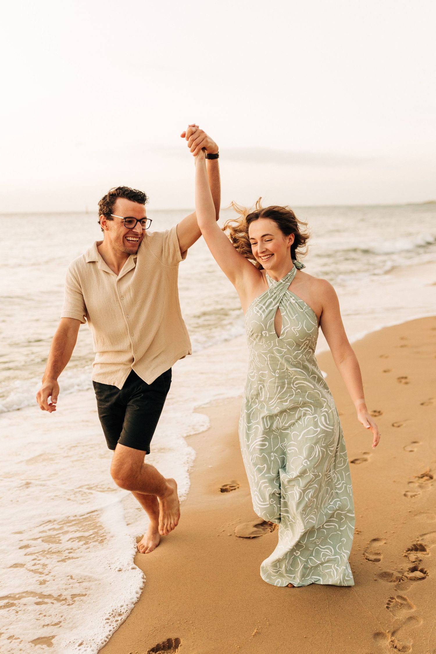 Joyful couple holding hands and running along a beach shoreline at sunset.